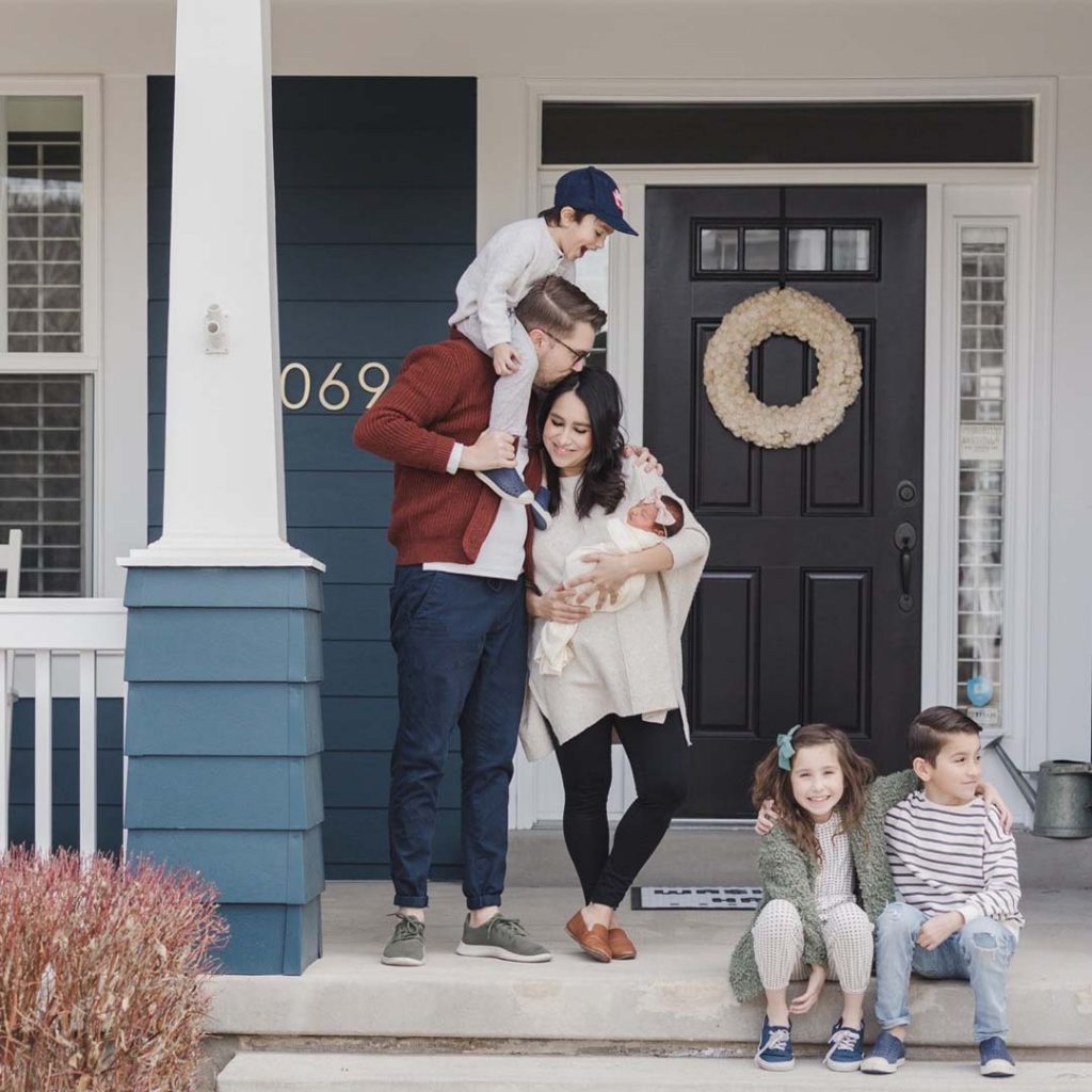 Family embraces on their front porch while holding new born baby in Daybreak.