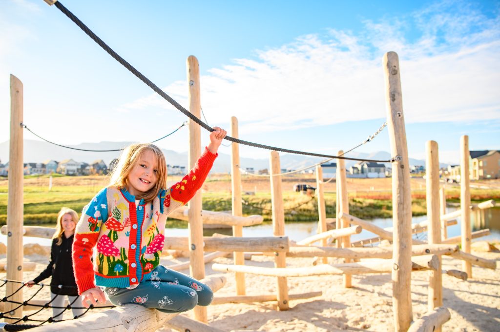 A little girl playing on a rope in Lookout Park's sand play area during daylight hours.