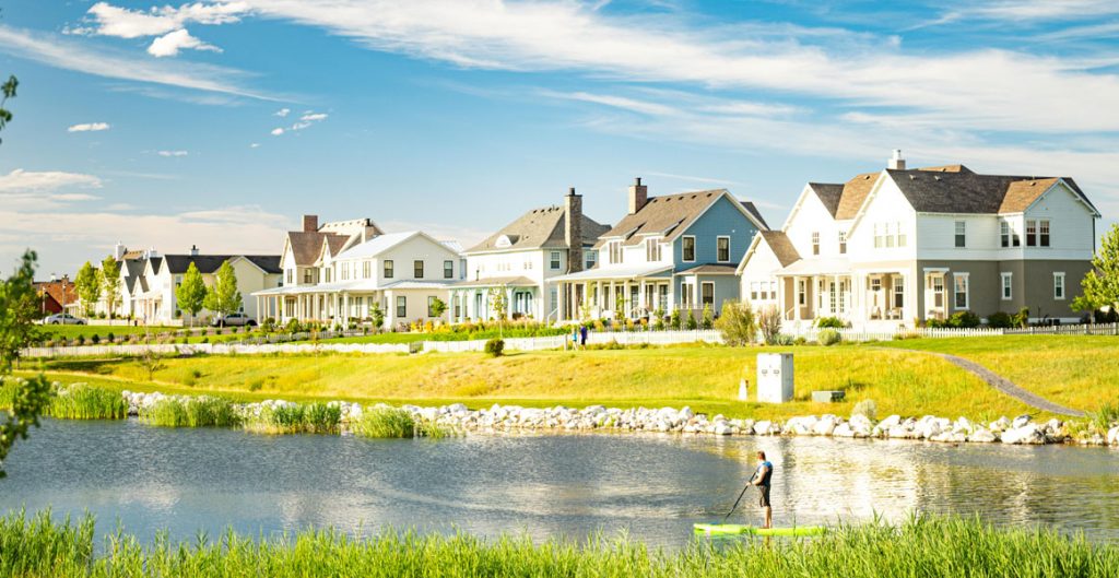 Daybreak home sales rose 40% YOY during 2020. Daybreak resident paddle boarding with new Daybreak homes in the background.
