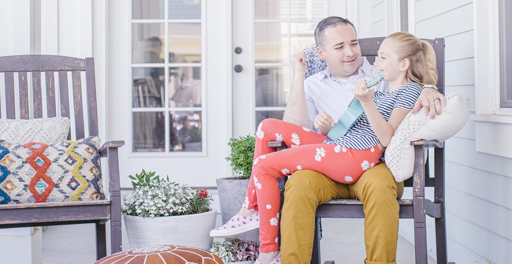 Dad and daughter sitting on the front porch of their new home